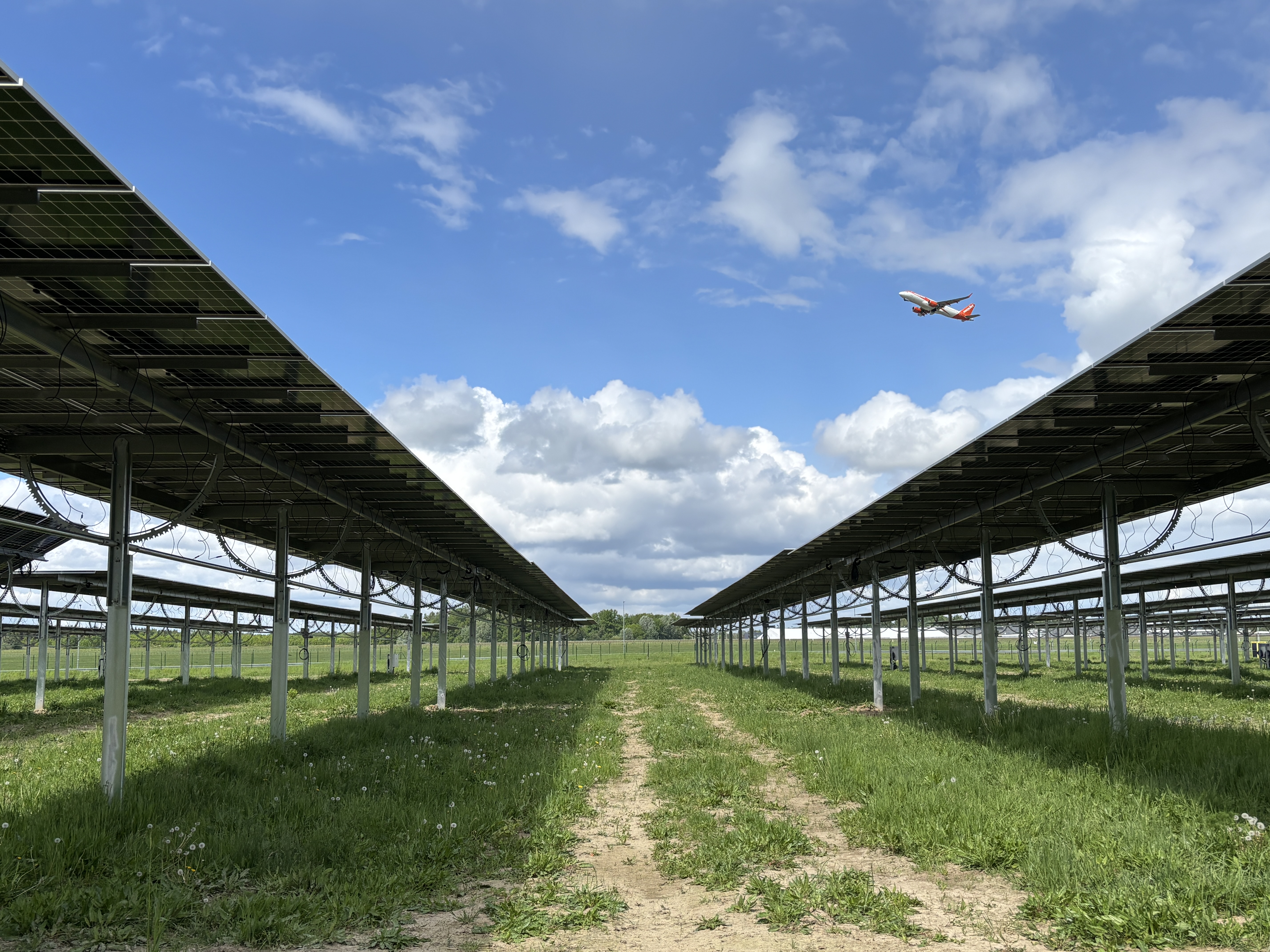 Startendes Flugzeug fliegt über aufgeständerte Solarpaneele.